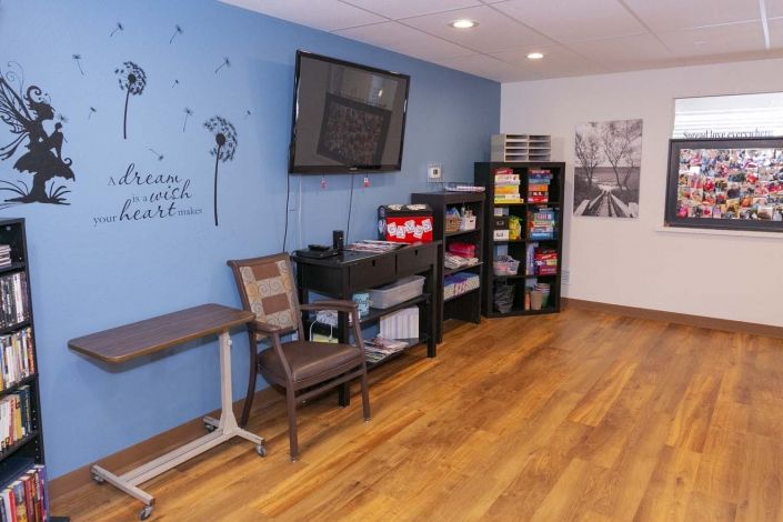 A cozy room with a wall-mounted television, shelves stocked with various items, and a comfortable chair on a hardwood floor.