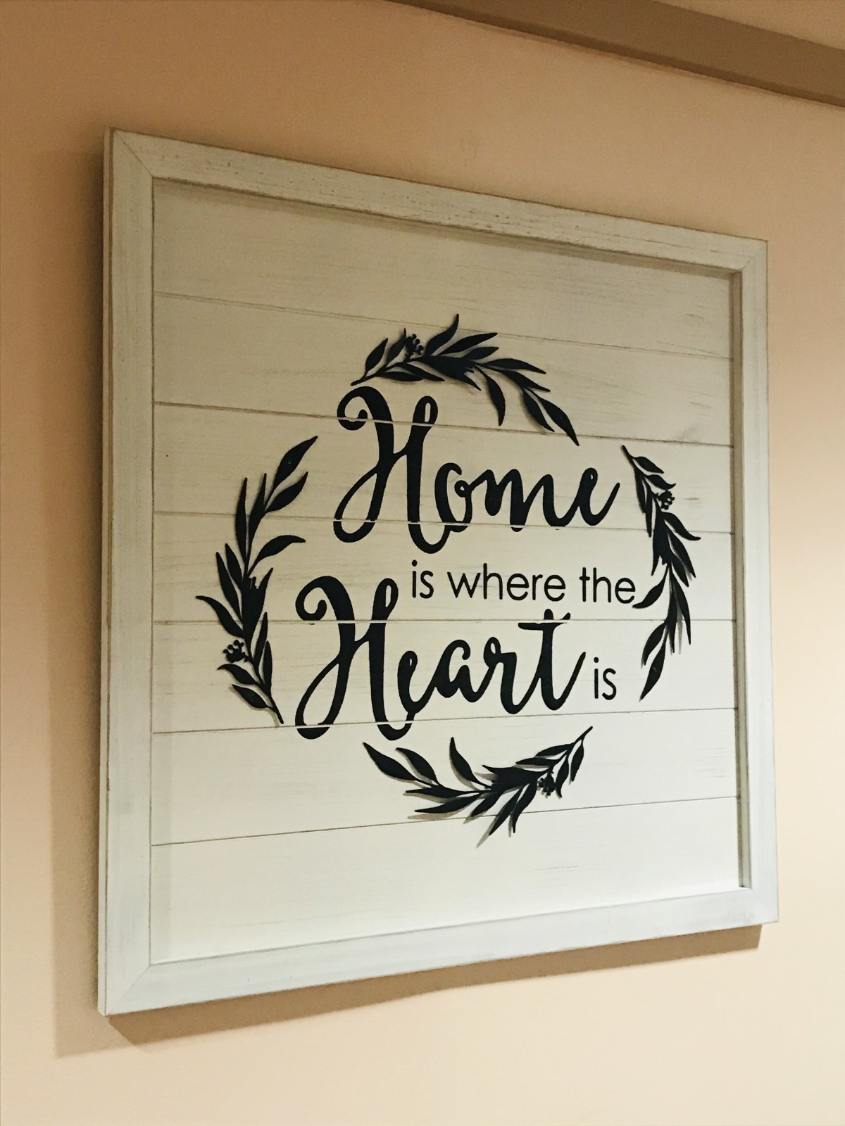 A framed wall art piece with the quote 'Home is where the heart is' surrounded by decorative leaves.