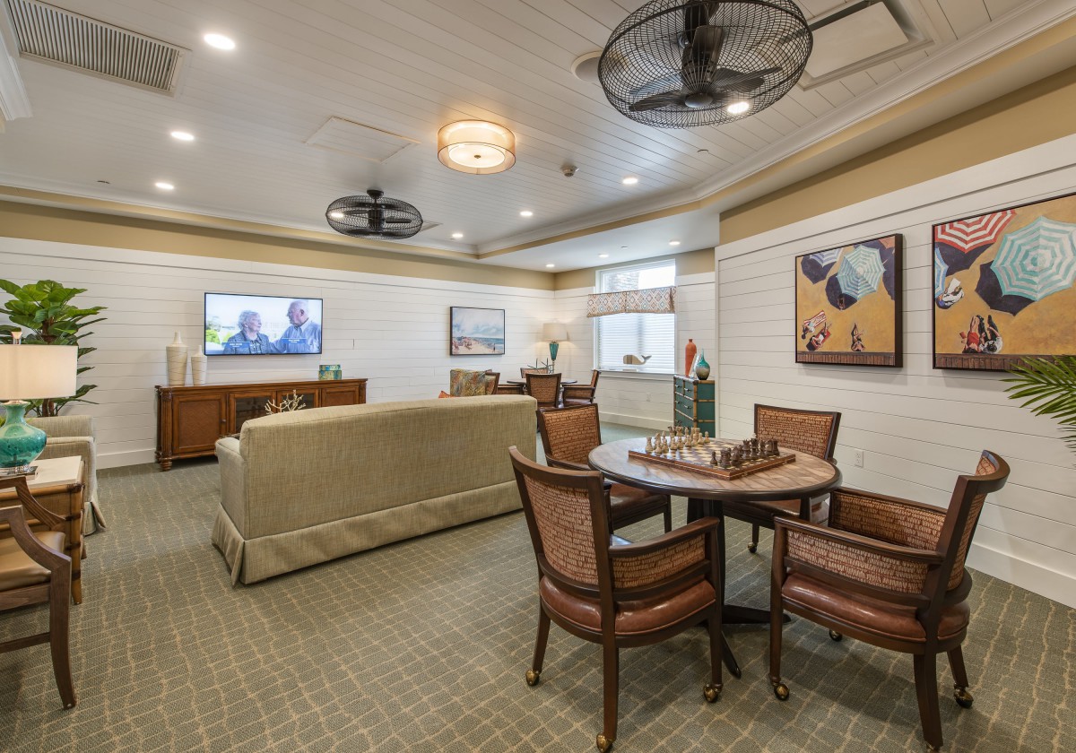 A cozy living room featuring a seating area with a chess board on the table, artwork on the walls, and a television.