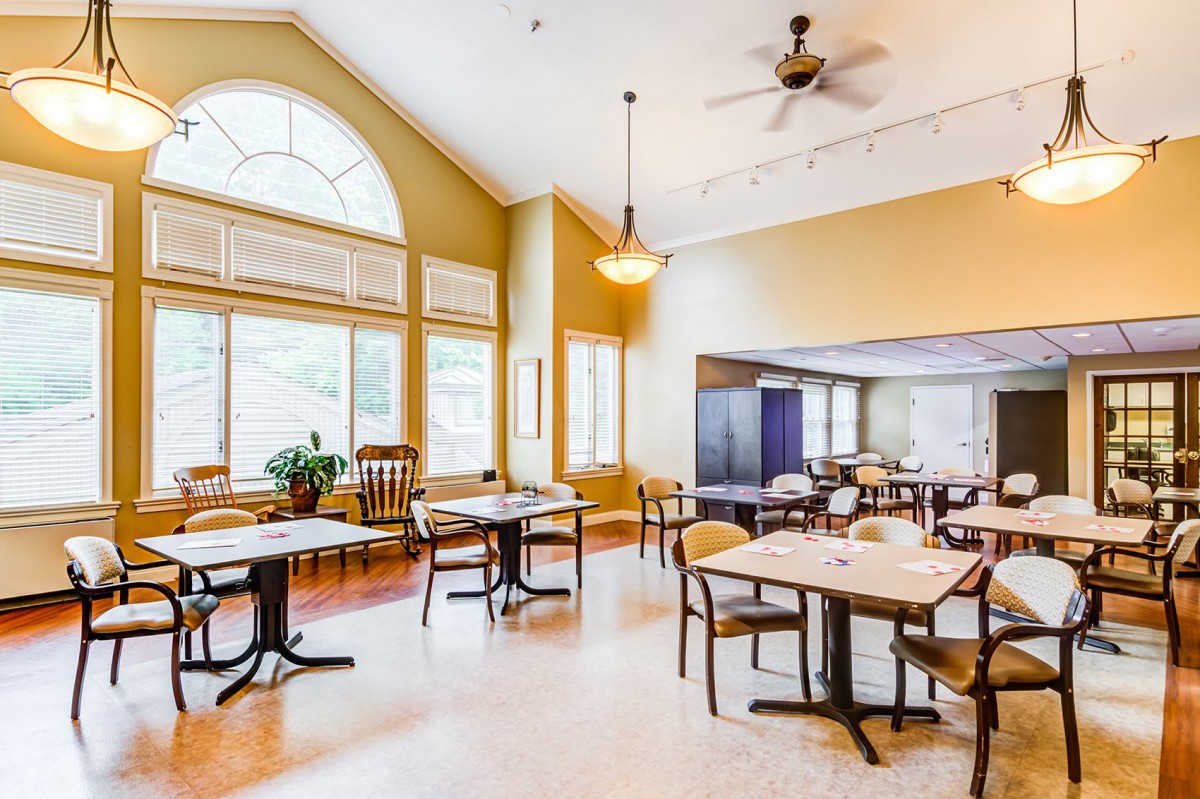 A bright and spacious dining area with multiple tables, chairs, large windows, and a ceiling fan.
