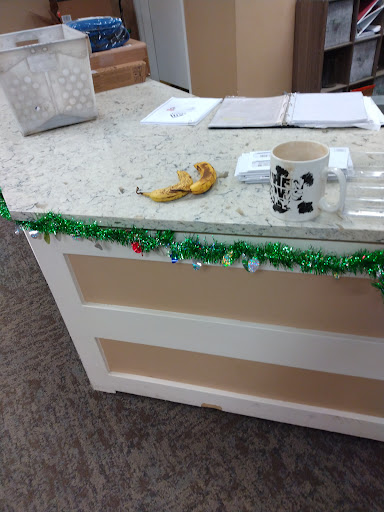 An office counter decorated with holiday garland, featuring a banana and a coffee mug.