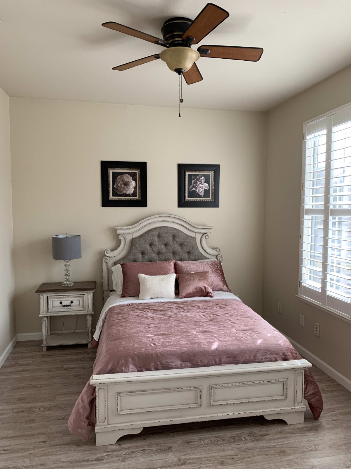 A cozy bedroom with a neatly made bed, bedside table with a lamp, and framed artwork on the wall.