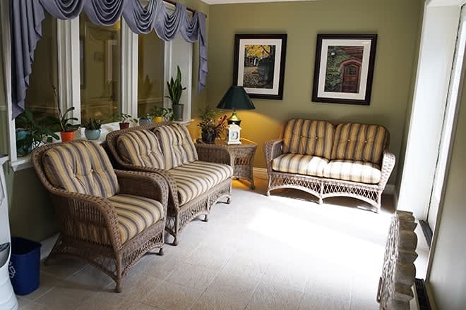 A cozy living room with wicker furniture and striped upholstery, featuring wall art and a table lamp by the window.