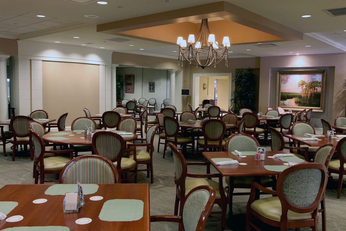 An elegant dining area with neatly arranged tables and chairs, illuminated by a chandelier.