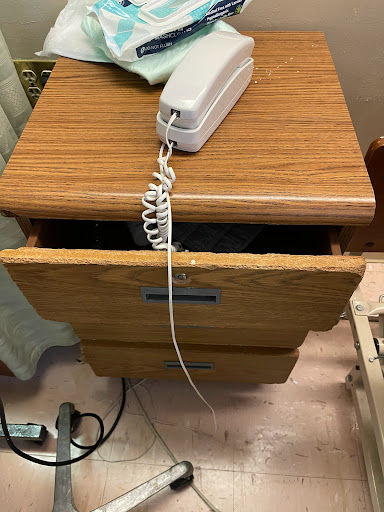 A wooden nightstand with a telephone resting on top and an open drawer.