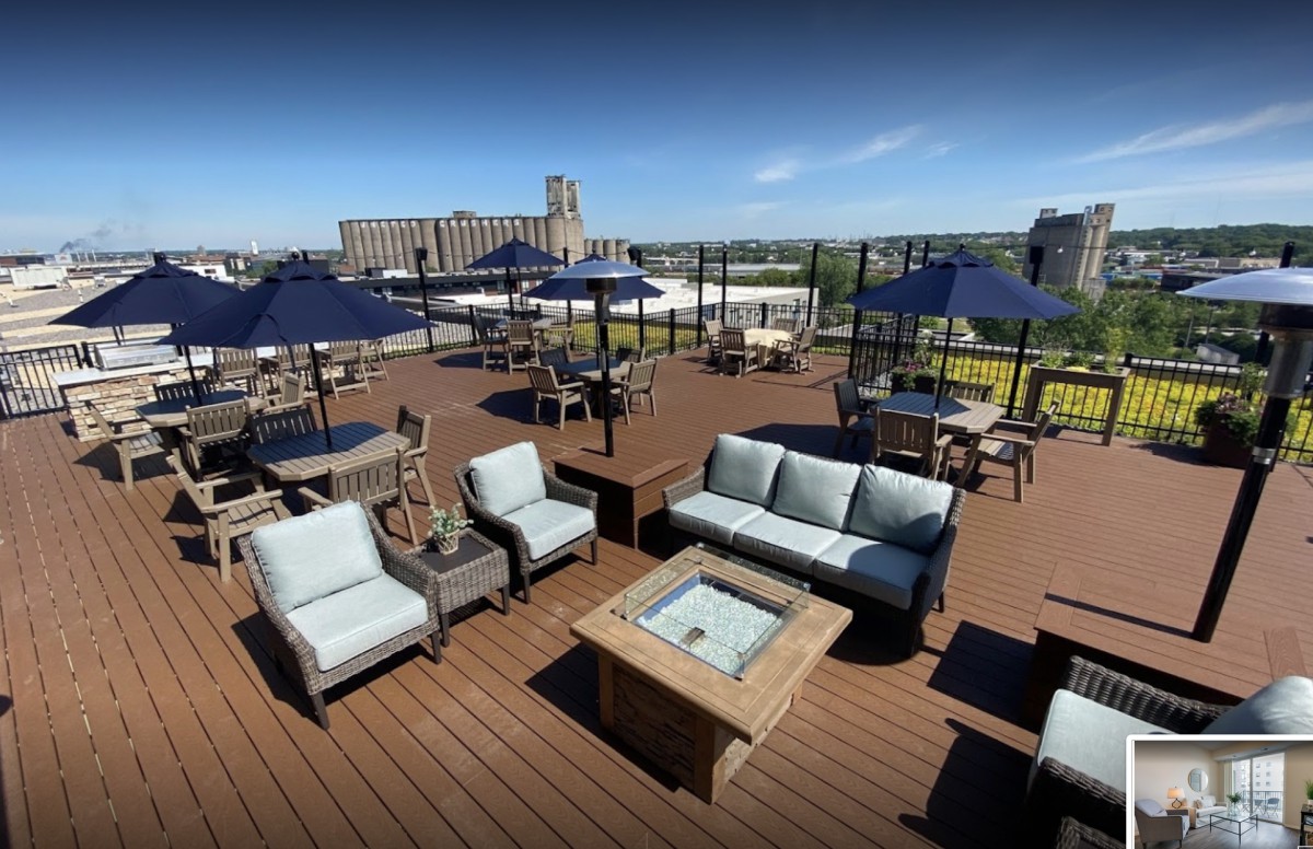 A spacious rooftop deck with comfortable outdoor seating and umbrellas, offering a scenic skyline view.