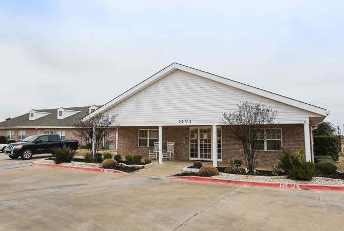 A suburban single-story brick building with a driveway and small shrubs.
