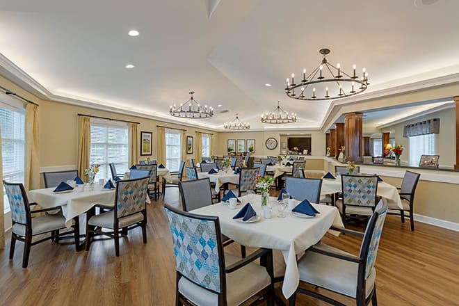 A spacious and elegantly decorated dining area with neatly arranged tables and chairs, illuminated by chandeliers.