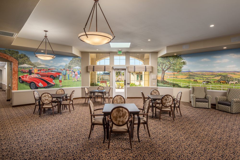 A cozy dining area with multiple tables and chairs, decorated with murals on the walls and illuminated by ceiling lights.
