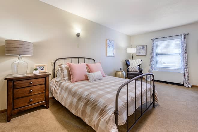 A cozy bedroom featuring an iron bed frame, decorative pillows, a wooden nightstand, and a comfortable reading chair by the window.