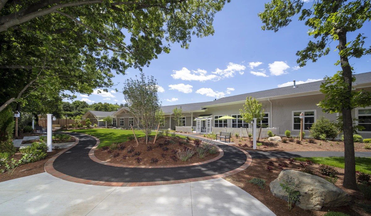 A modern building surrounded by a landscaped garden with trees and a paved walkway under a clear blue sky.