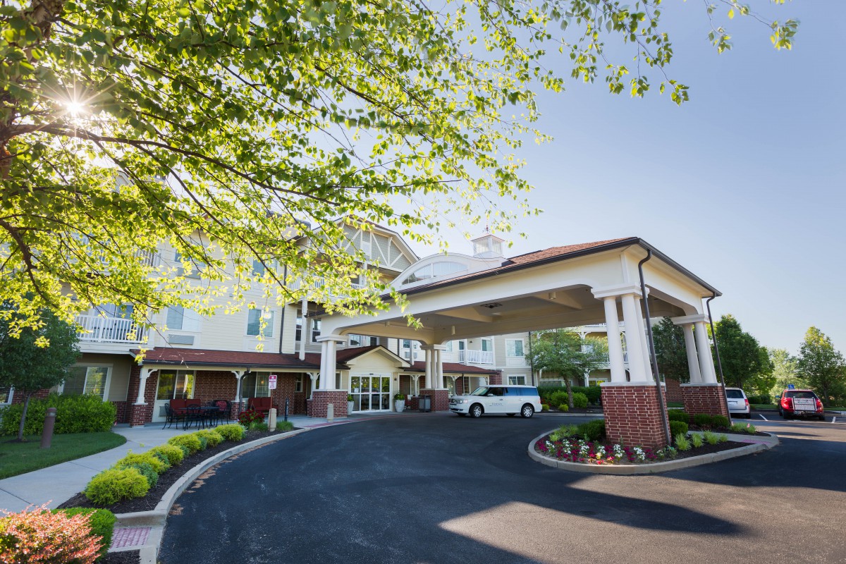 A building entrance with a covered driveway and landscaping under sunny skies.