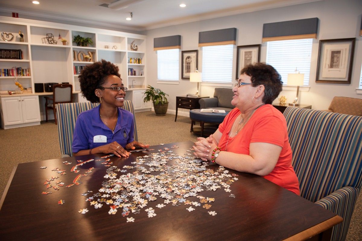 Two people sitting at a table working on a puzzle together, engaged in conversation.