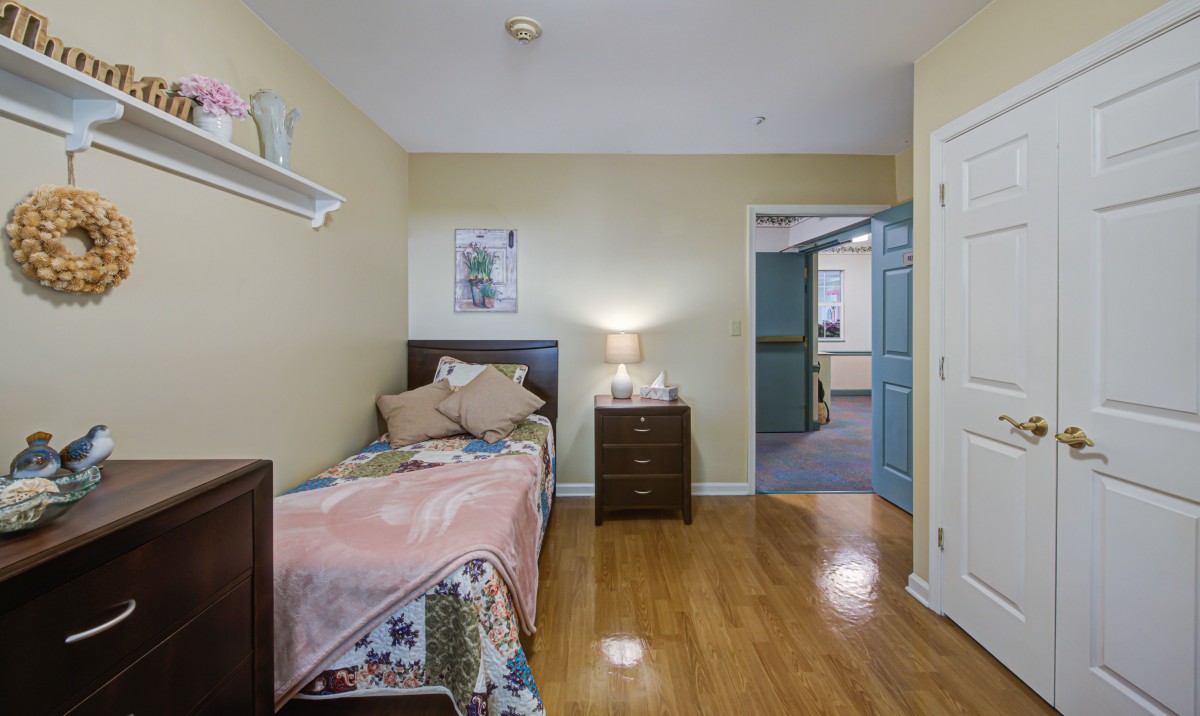 A cozy bedroom with a single bed, nightstand, and lamp on a hardwood floor.