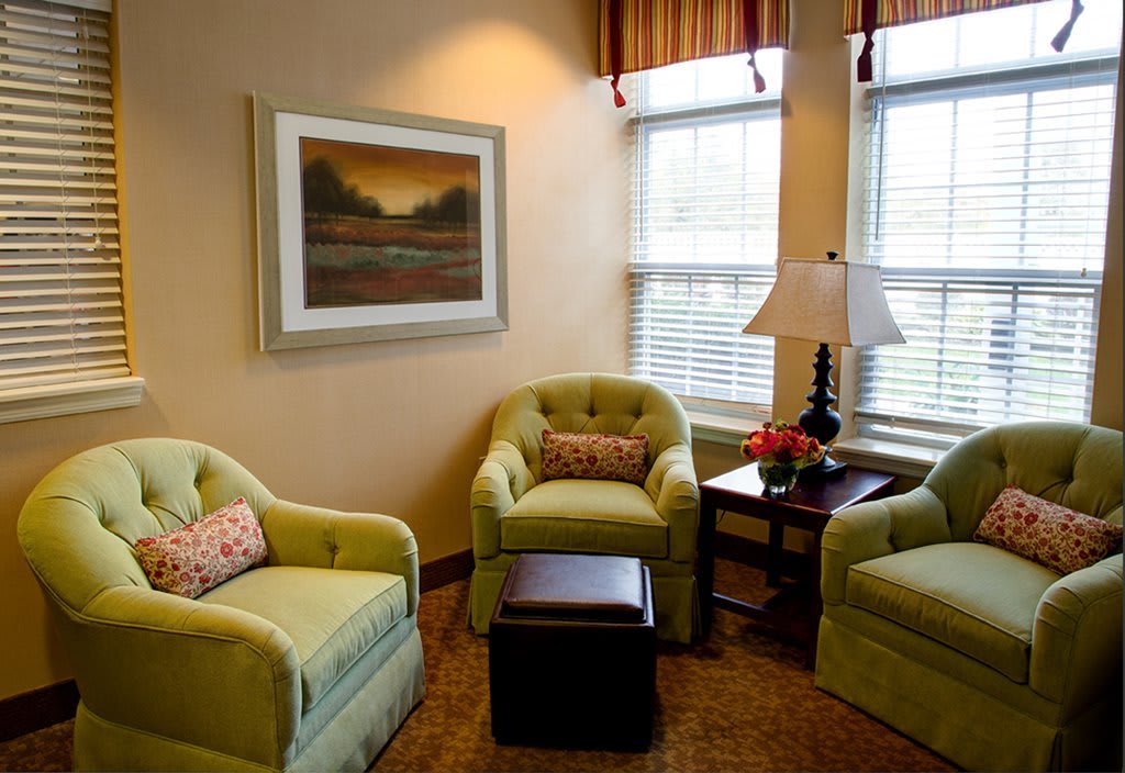 A cozy living room corner with three green armchairs, a lamp, and wall art.