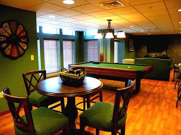 A cozy game room featuring a pool table and wooden furniture, accented by warm lighting.