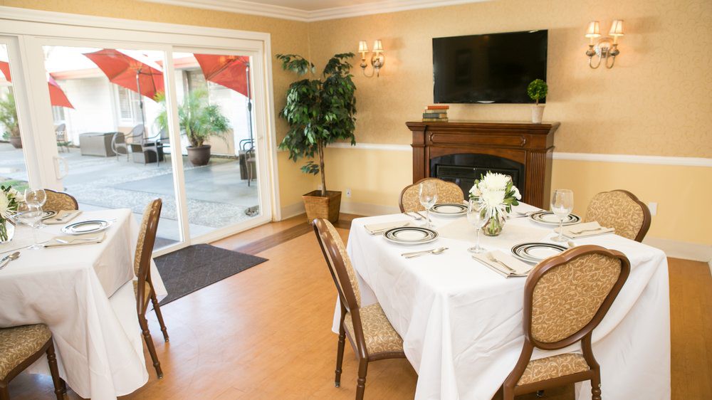 A cozy dining room with a beautifully set table, fireplace, and large windows looking out to a patio.