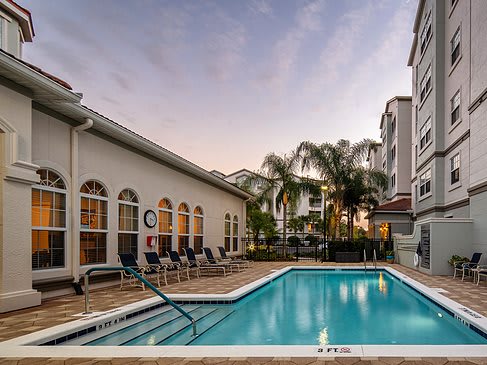 A serene poolside view in a residential area at sunset, surrounded by palm trees and buildings.