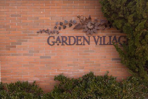 A sign reading 'Garden Village' on a brick wall, surrounded by greenery.