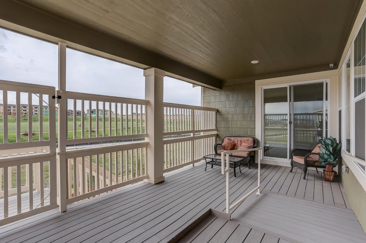 A cozy covered porch with outdoor seating, featuring wooden flooring and railing.