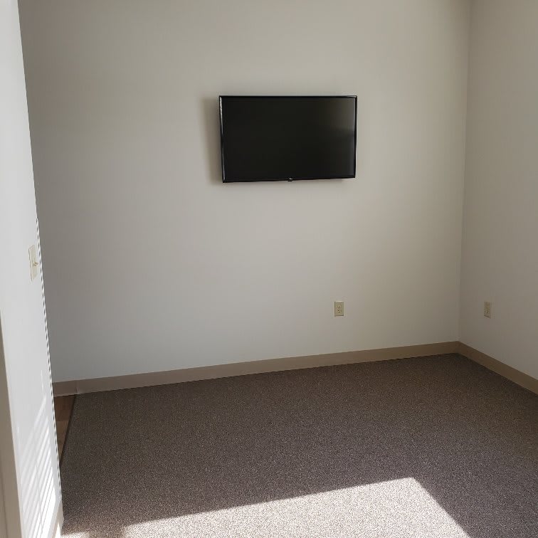 A minimalist empty room with a wall-mounted television and carpeted floor.