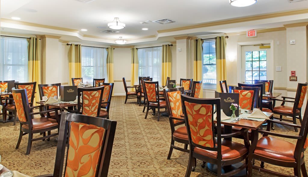 An elegant dining room with multiple tables and chairs, featuring warm d�cor and natural light from large windows.