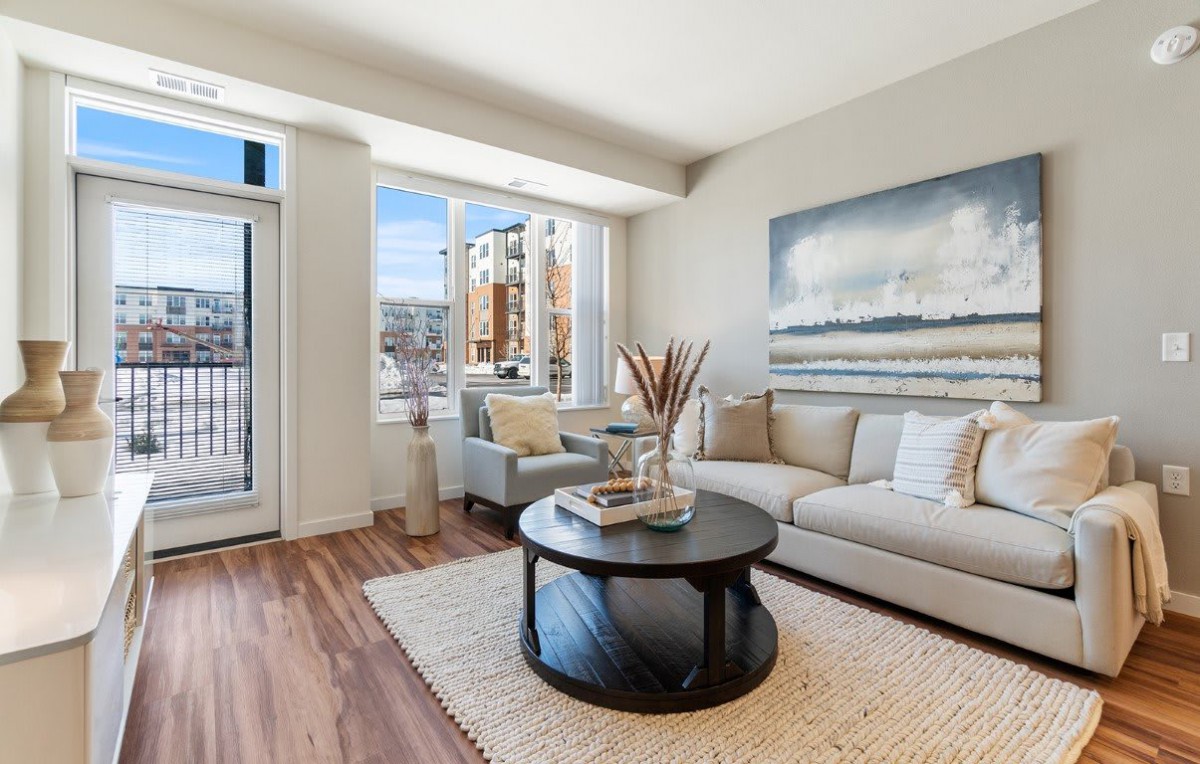 A modern living room with a comfortable sofa, round coffee table, and large artwork on the wall, illuminated by natural light from large windows.