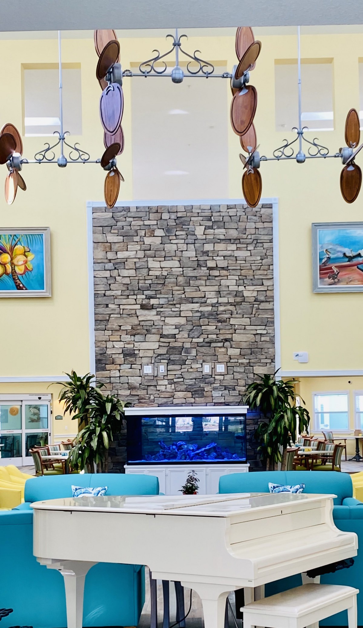 A spacious lobby featuring a large stone fireplace, an aquarium, tropical plants, and decorative artwork on the walls.
