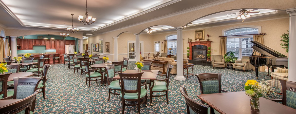 A spacious and elegantly decorated dining area with multiple tables and chairs, featuring classic interior design elements and ambient lighting.