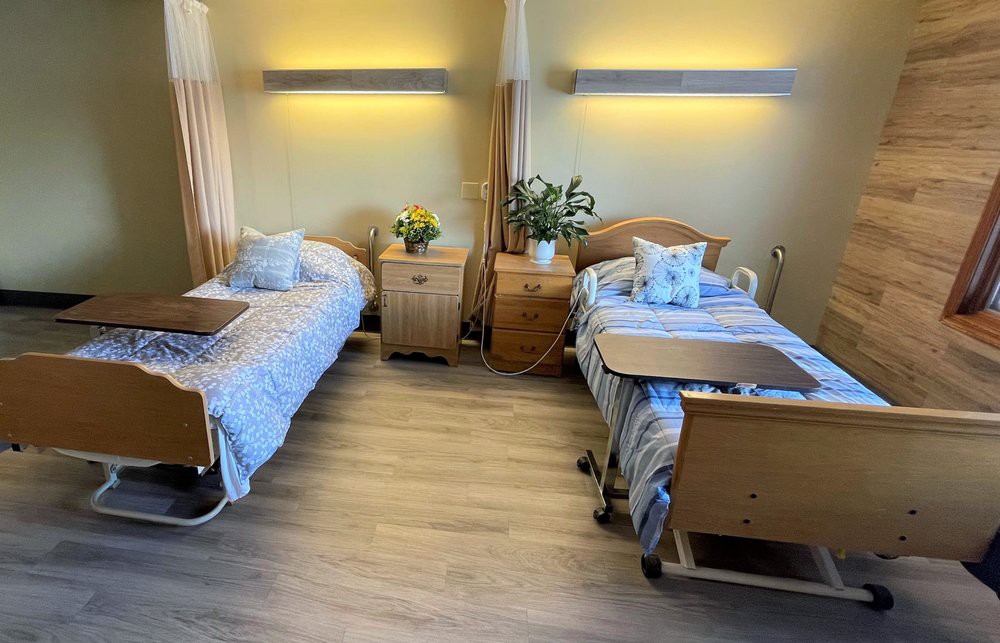 A hospital room with two beds, bedside tables, and decorative plants.