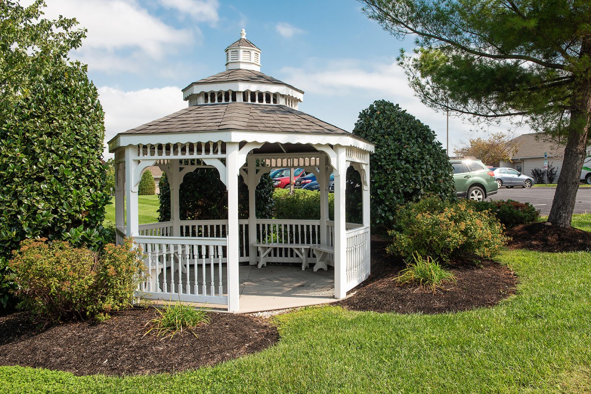 A picturesque white gazebo surrounded by lush green grass and shrubs.