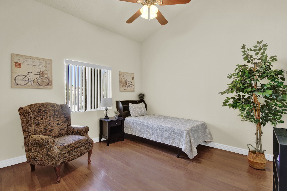 A cozy bedroom with a single bed, armchair, nightstand, and ceiling fan.