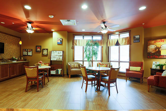 A cozy lounge area with tables and chairs, featuring large windows and tasteful decor.