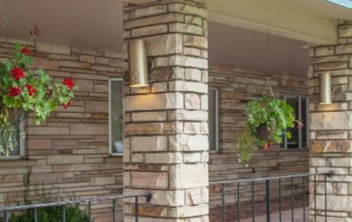 A cozy porch featuring a stone column with a light fixture and hanging plants against a brick wall backdrop.