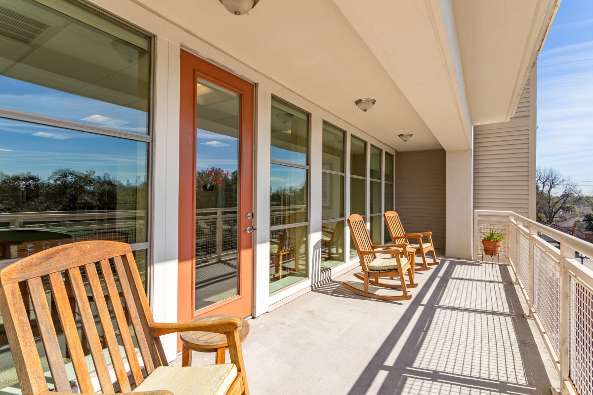 A sunny porch with wooden rocking chairs and large glass doors.