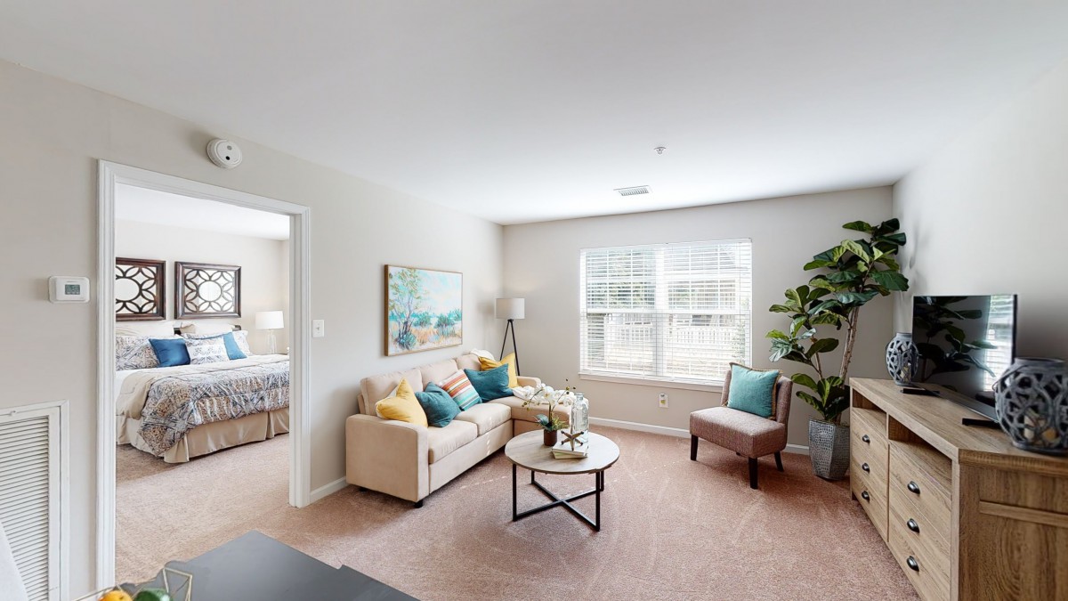 A bright and cozy living room with a beige sofa, colorful pillows, and a round coffee table near the window.