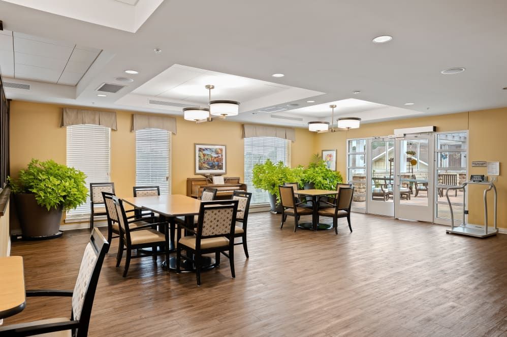 A spacious dining area with wooden flooring, tables, chairs, and large windows allowing natural light.