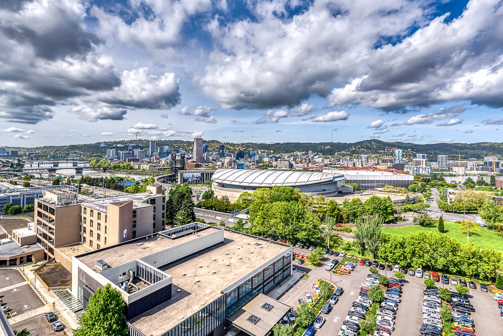 A vibrant cityscape featuring a mix of urban buildings and lush greenery under a partly cloudy sky.