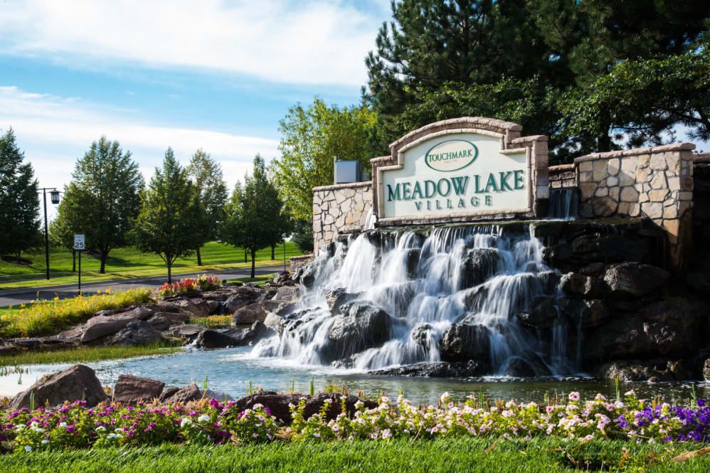 Entrance to Meadow Lake Village with a scenic waterfall and lush greenery.