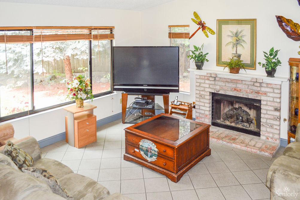 A cozy living room featuring a large television, a wooden coffee table, and a fireplace surrounded by decorative elements.