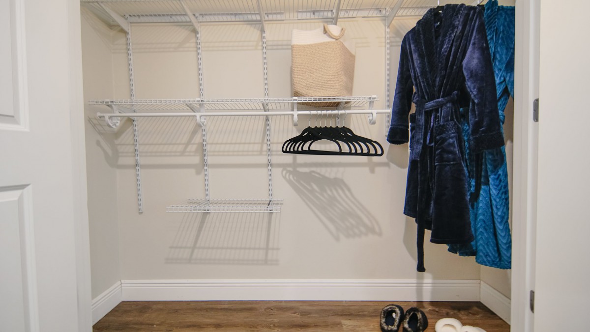 An organized closet with empty shelves, hangers, and a robe hanging neatly.