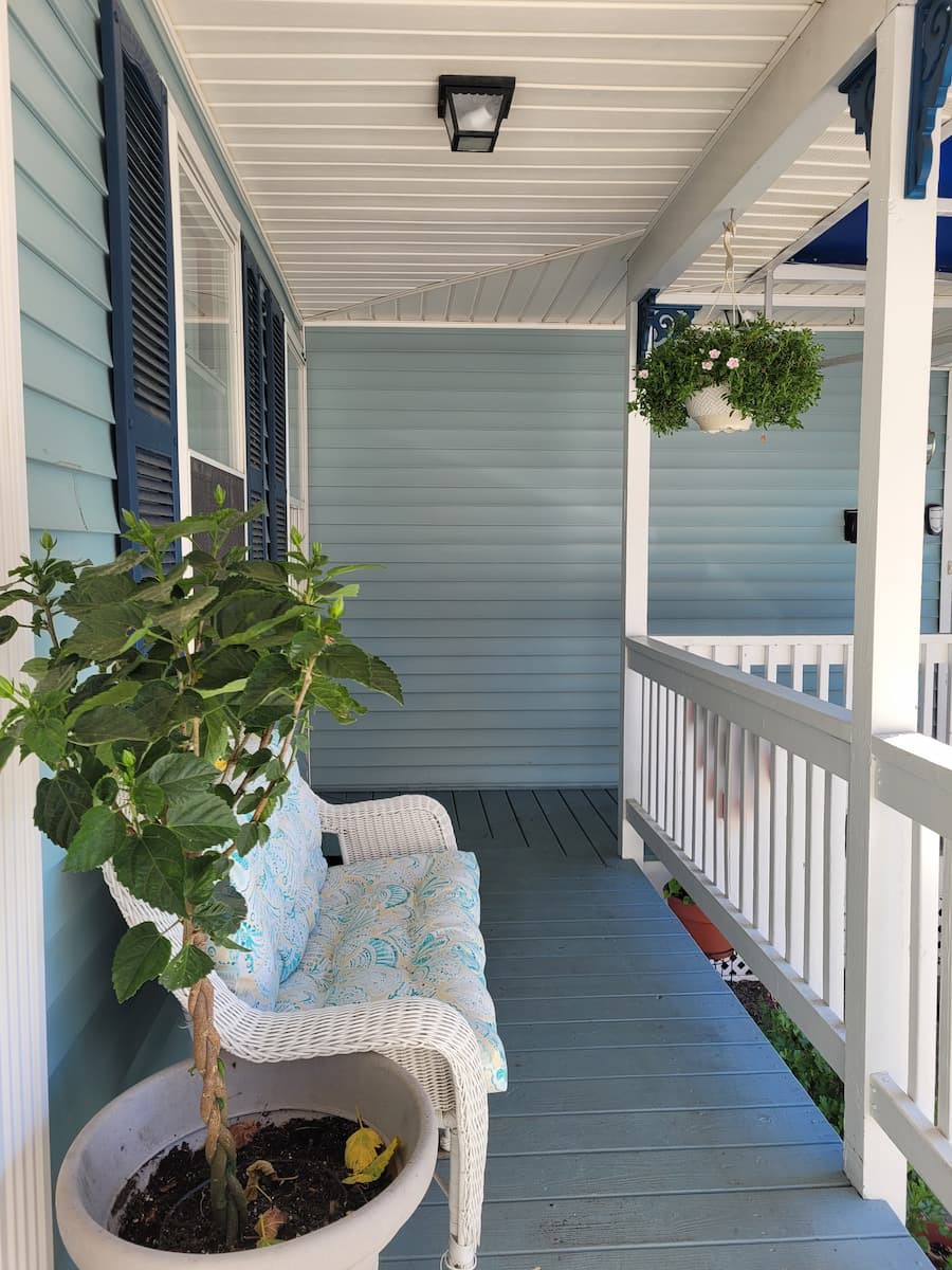 A cozy porch with a white bench, a potted plant, and a hanging plant.