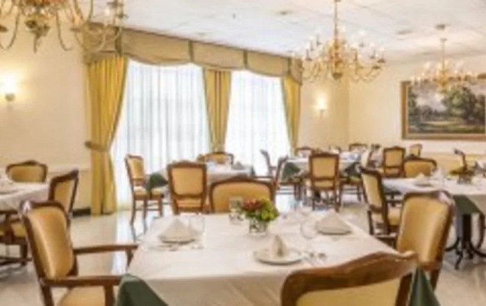An elegant dining room with chandeliers, drapes, and a neatly set table.