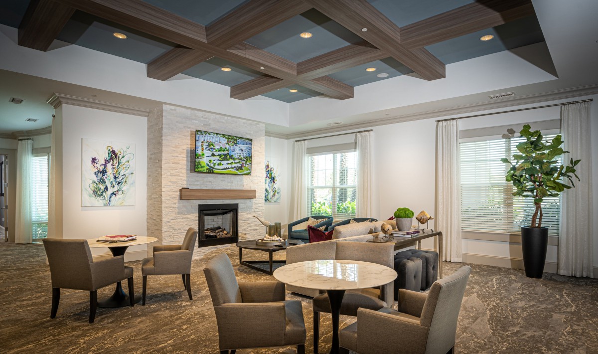 A modern living room featuring a cozy seating area with tables, chairs, a fireplace, and a television mounted above.