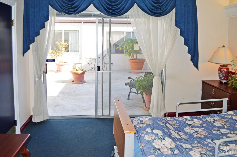 A cozy bedroom with blue and white decor, featuring a sliding glass door opening to a patio with potted plants.