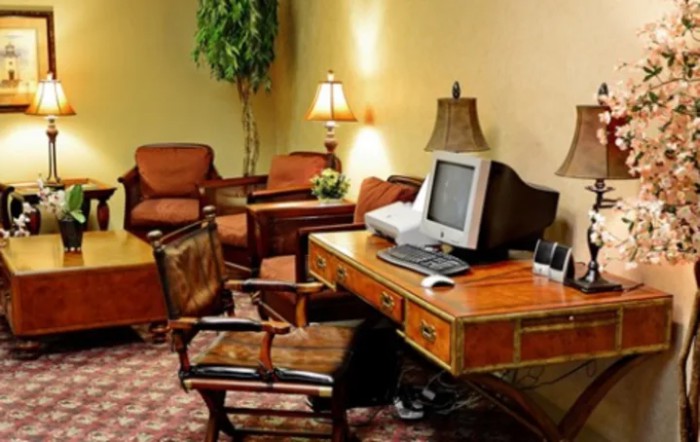 A vintage office setup with a wooden desk and an old computer, surrounded by comfortable chairs and warm lighting.