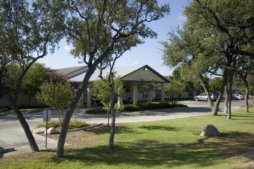 A sunny day with a view of a building surrounded by trees and a well-maintained lawn.