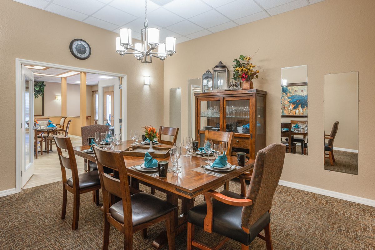 A well-appointed dining room with a set dining table, surrounded by wooden chairs and illuminated by a chandelier.