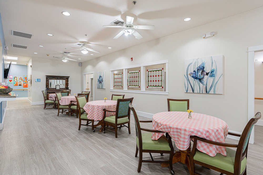A modern dining area with neatly arranged tables and chairs, featuring ceiling fans and decorative artwork on the walls.
