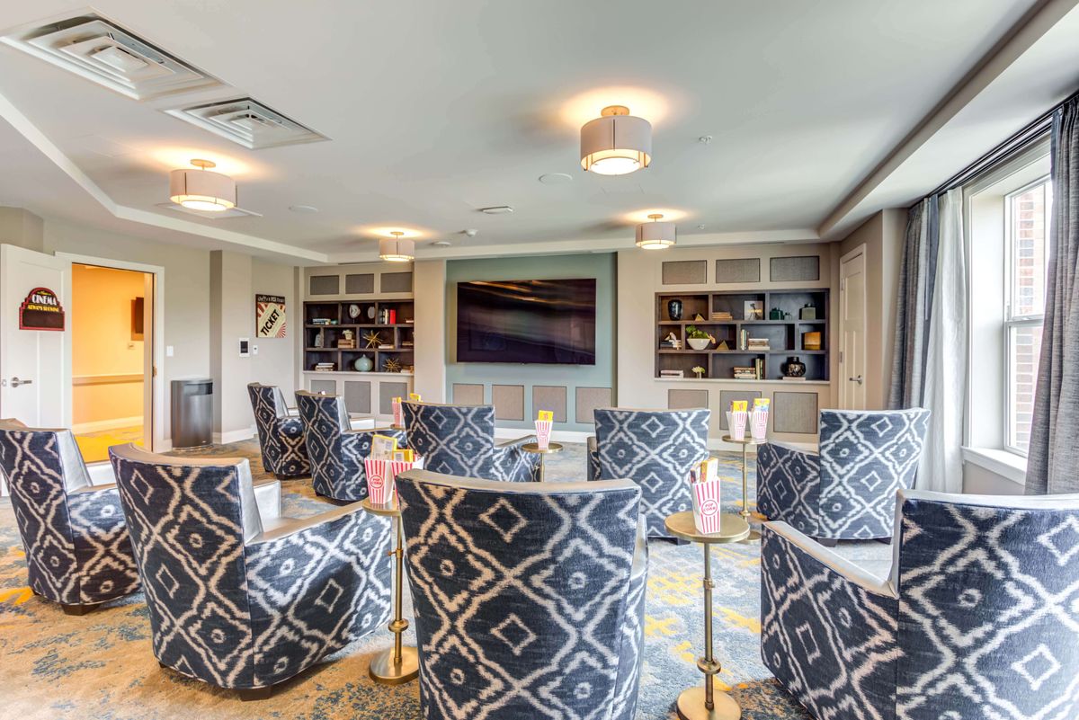 A modern lounge with patterned chairs, built-in bookshelves, and a large television.
